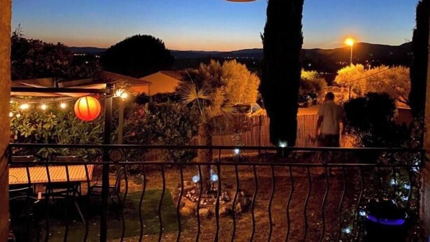 Un balcon donnant sur un jardin, un grand arbre et une chaîne de montagnes lointaine.