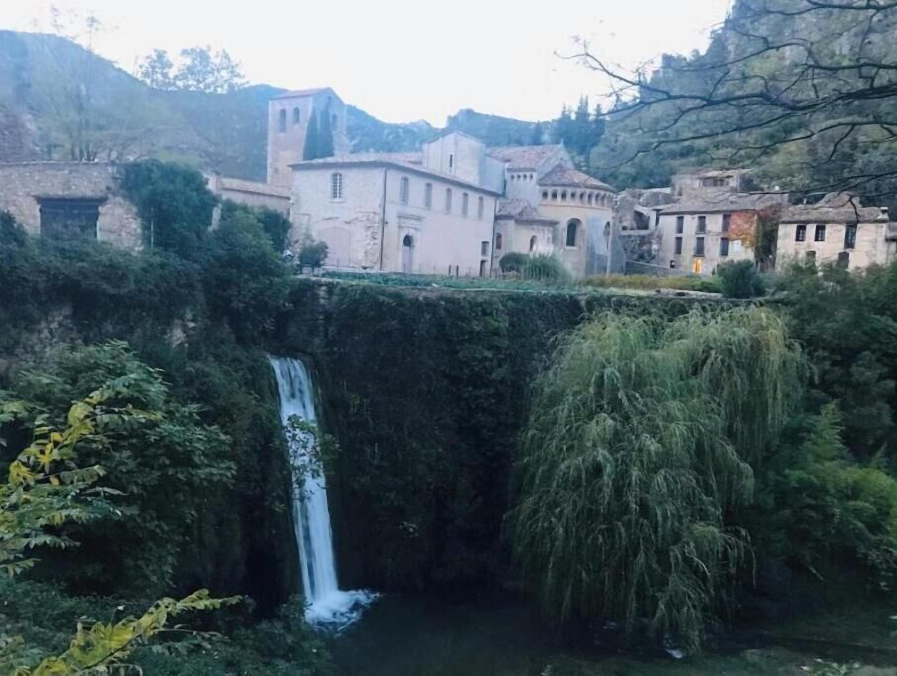 Uma cascata rodeada por vegetação exuberante e edifícios históricos.