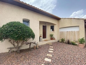 A house with a gravel driveway, a small tree, and a wooden bench.