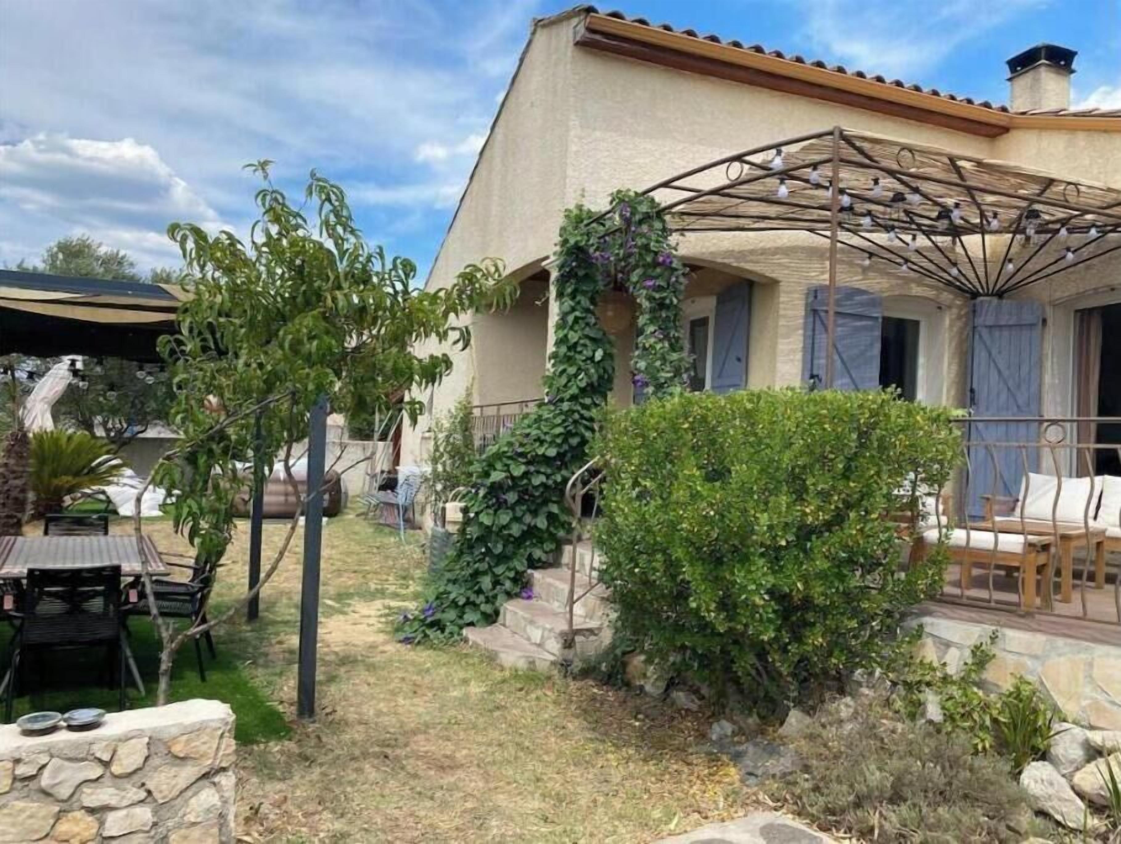 Una casa con patio, mobiliario exterior y una pérgola.