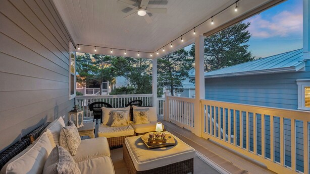 A covered porch with a ceiling fan, string lights, wicker furniture, and a view of a blue house. - Community Pool and Hot Tub Access | LSV (Santa Rosa Beach)