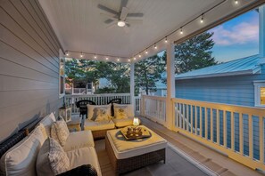 A covered porch with a ceiling fan, string lights, wicker furniture, and a view of a blue house. - Community Pool and Hot Tub Access | LSV (Santa Rosa Beach)