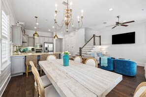 Eine moderne Küche mit weißen Schränken, ein Essbereich mit Holztisch und ein Wohnzimmer mit blauen Sofas.