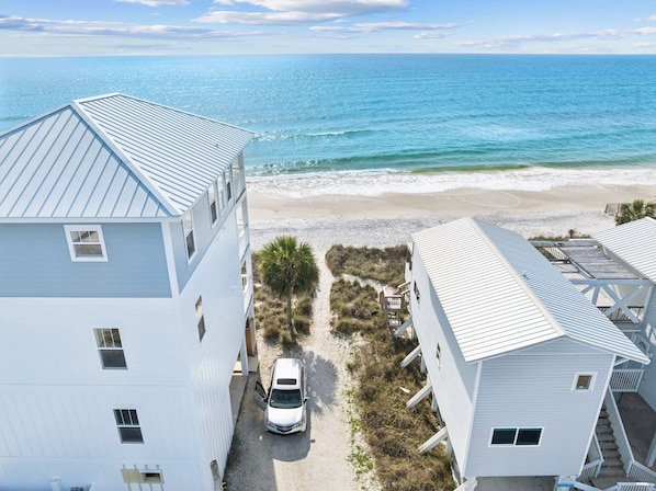 A coastal building complex with a beach view, a car parked in front, and a clear sky.