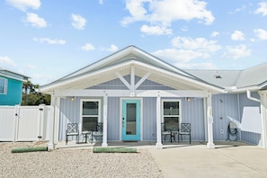 A building with a covered patio area, a door, and two chairs.
