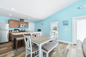 A modern kitchen with wooden cabinets, a central island, and a dining area with white chairs and a bench.