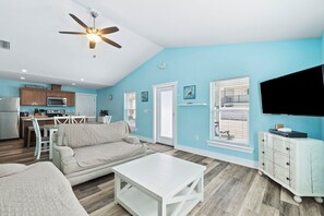 A living room with a sofa, coffee table, TV, and kitchen area with cabinets and appliances. - Duplex with Private Pool, Grill, Arcade and Backyard (Port St. Joe)