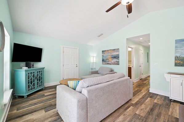 A living room with a sofa, a television, a cabinet, and a ceiling fan. - Large Group Escape with Pool and Spa (Port St. Joe)