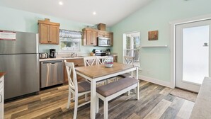 Una cocina moderna con electrodomésticos de acero inoxidable, armarios de madera y un comedor con sillas blancas y una mesa de madera.