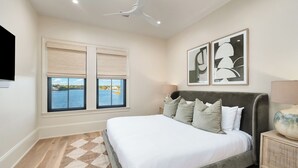 Un dormitorio con cama, ventilador de techo, ventana con persianas y dos cuadros en la pared.