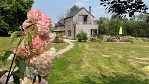 Una casa de madera con balcón, rodeada de un césped cuidado y plantas en flor.