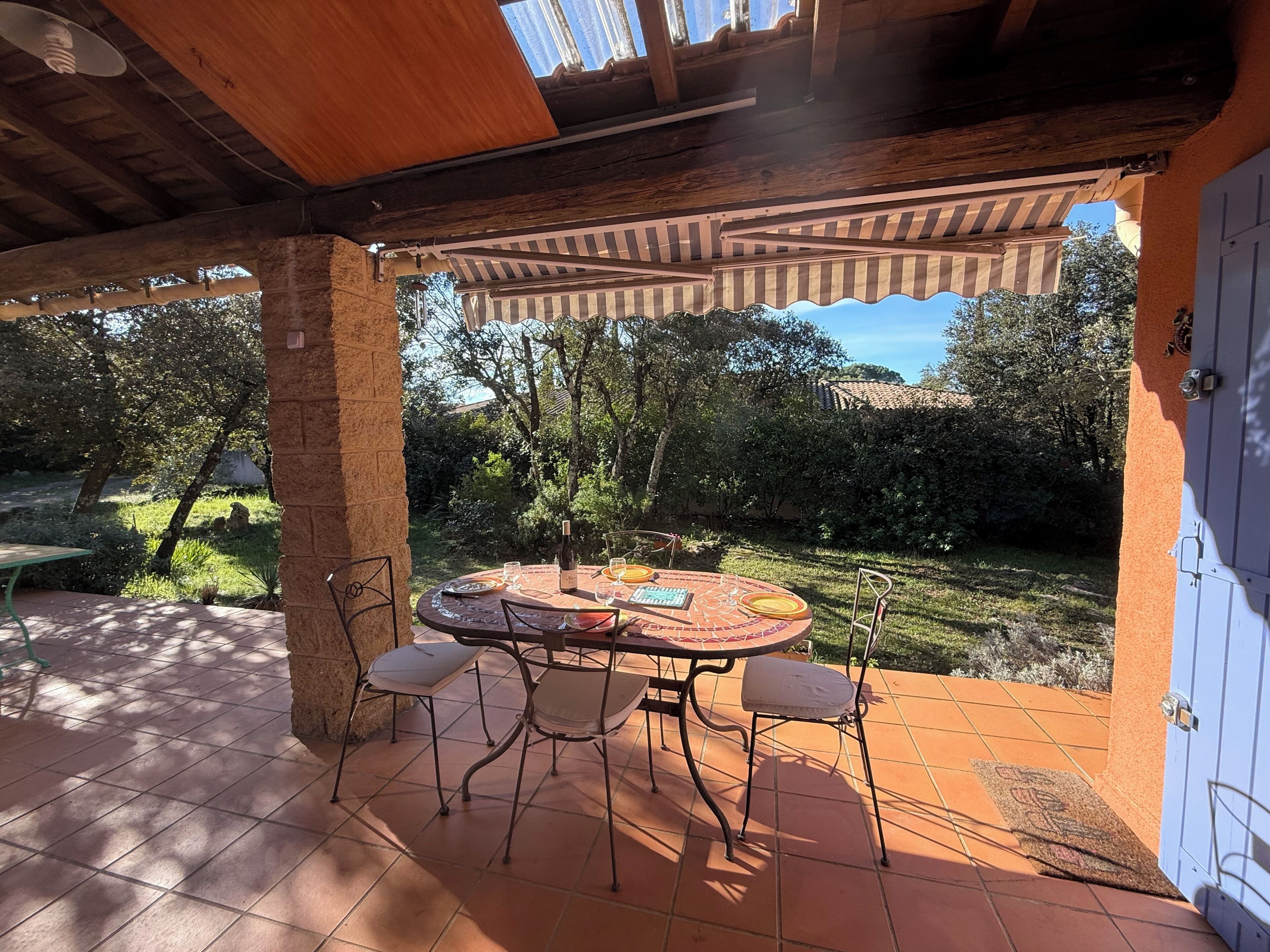 A covered patio with a round table and chairs, a tiled floor, and a view of a garden.