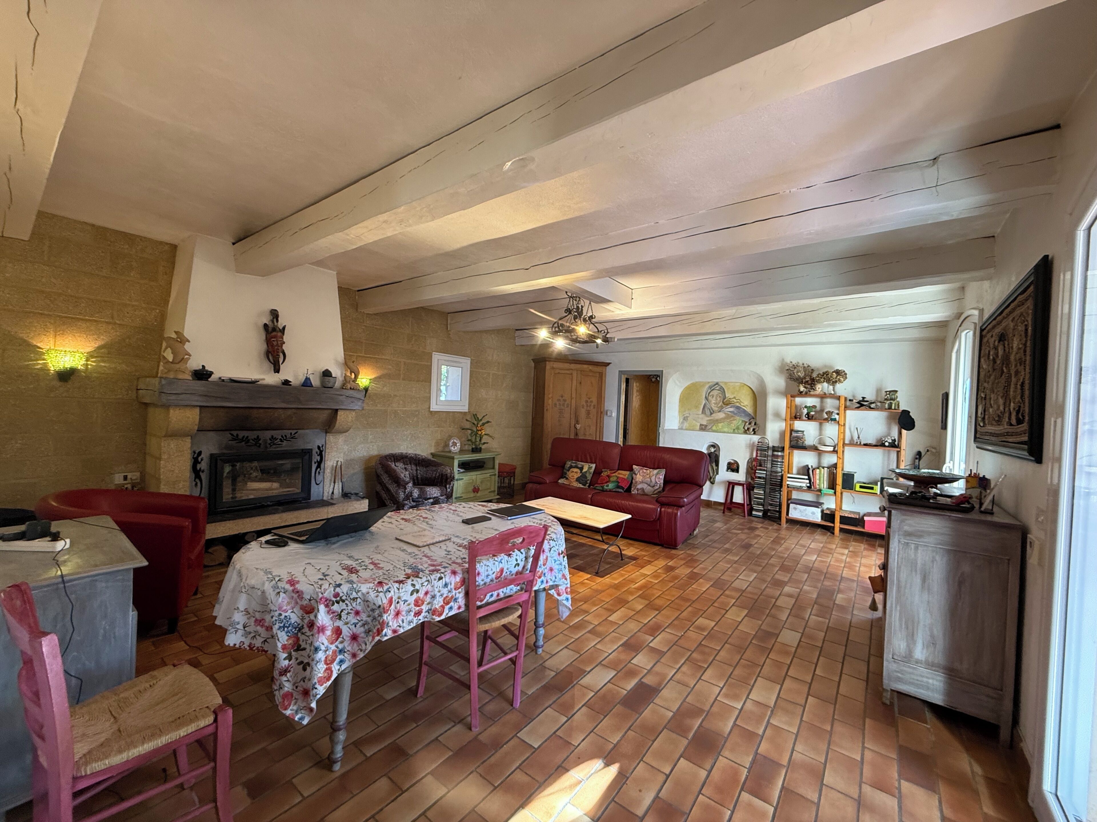 A cozy living room with a fireplace, a red sofa, a dining table with chairs, and a bookshelf.