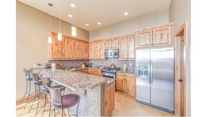 A kitchen with wooden cabinets, a stainless steel refrigerator, granite countertops, and bar stools. - LUXURY 4-BED 5-BATH VILLA ACROSS FROM Mt CB BASE, SLEEPS 12 (Crested Butte)