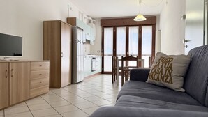 En moderne stue med sofa, fjernsyn, et køkken og et spisebord.