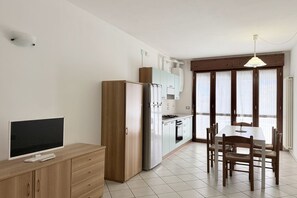 Une cuisine moderne avec un coin repas, un téléviseur posé sur un meuble en bois et une fenêtre avec des rideaux.