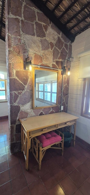 A room with a stone wall, a wooden table with a mirror, and a bench with a pink cushion. - SS 10 (10A y 10B) Cabaña rustica frente al malecón de La Paz (La Paz)