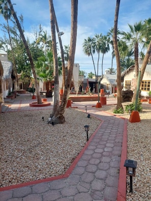 A courtyard with palm trees, a gravel path, and buildings with thatched roofs. - SS 10 (10A y 10B) Cabaña rustica frente al malecón de La Paz (La Paz)