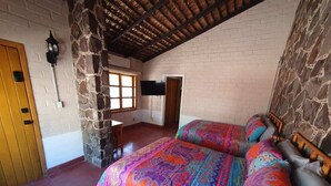 A bedroom with a stone wall, a wooden door, a bed with colorful bedding, and a TV mounted on the wall. - SS 6 (6A y 6B) Cabaña rustica frente al malecón de La Paz (La Paz)