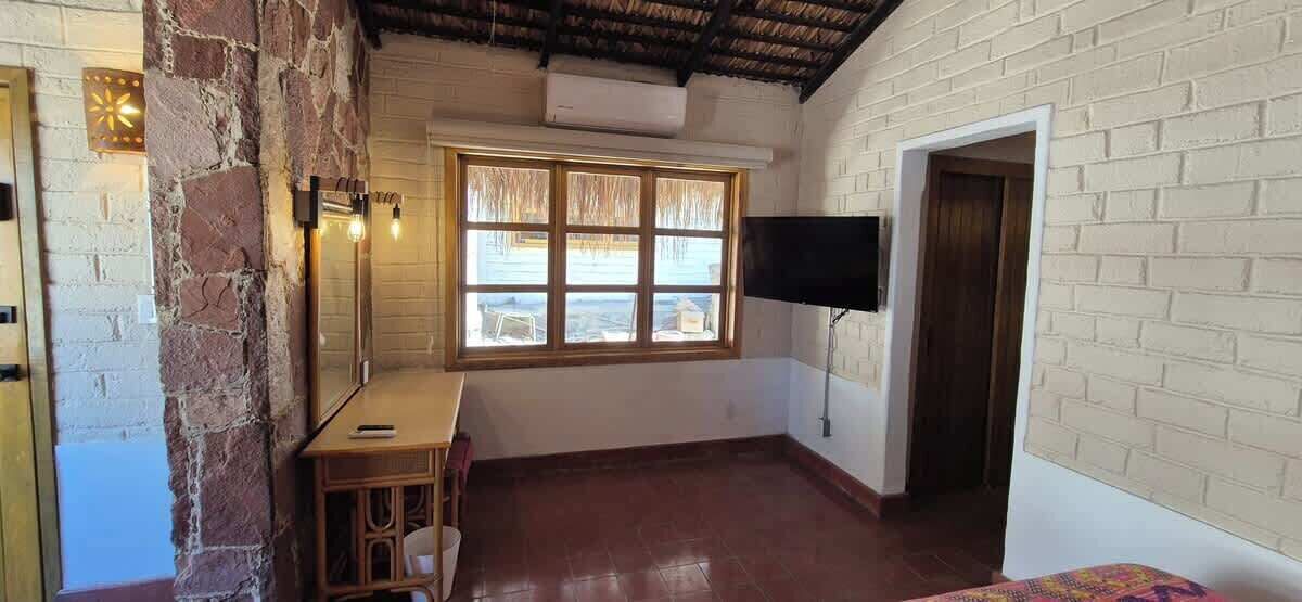 A room with a stone wall, a wooden desk, a window, a flat-screen TV, and a door.