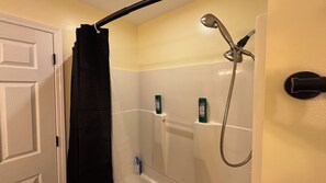 Une douche équipée d’un pommeau de douche amovible, d’un porte-serviettes et de deux bouteilles de shampoing fixées au mur.
