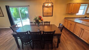 Un espace repas comprenant une table, des chaises, un vase avec des fleurs, un lustre et des meubles de rangement en bois.