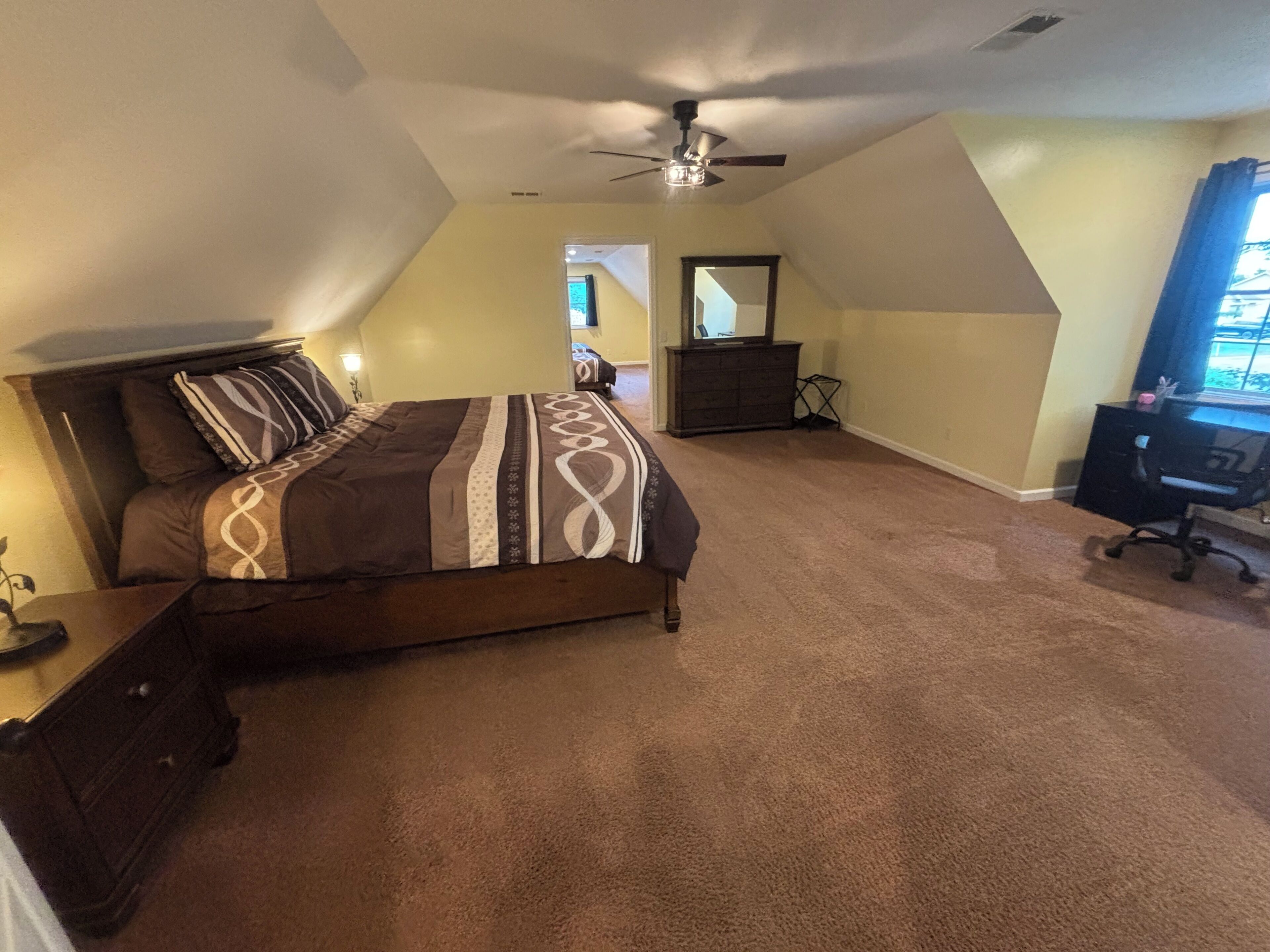 Une chambre à coucher comprenant un lit, une commode, un bureau et un ventilateur de plafond.