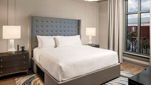 Een hotelkamer met een groot bed, twee nachtkastjes met lampen, een raam met gordijnen en uitzicht op gebouwen.