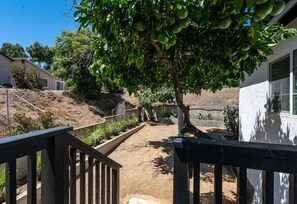 Una propiedad residencial con entrada pavimentada, cerca de madera y un árbol de hojas verdes.