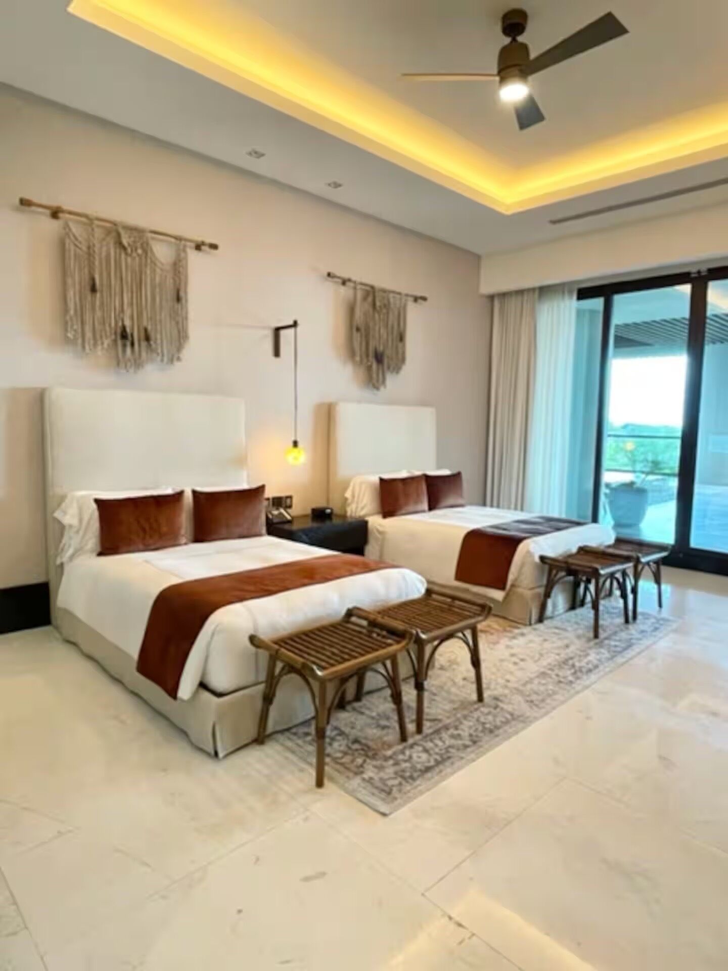 A hotel room with two beds, a ceiling fan, a large window, and a view of the outdoors.