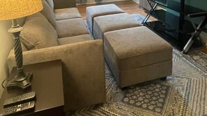 Ein Wohnzimmer mit Sofa, Hocker, Fernseher, Lampe und Heizkörper.