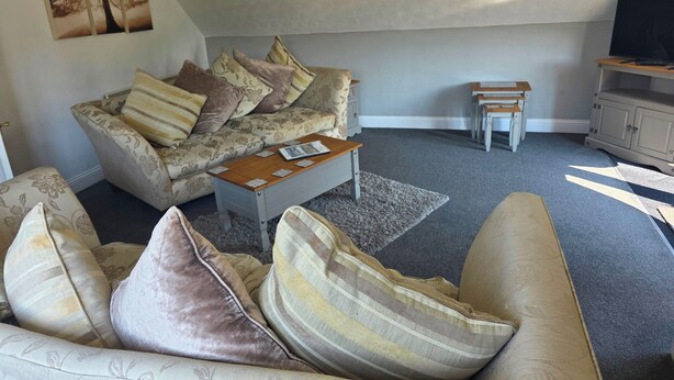 A living room with a sofa, armchair, coffee table, and a television. - Lakeview Villa (Liskeard)