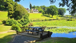 A picnic area with a table and benches, surrounded by a pond with lily pads and greenery. - Lakeview Villa (Liskeard)