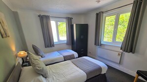 A room with two beds, a wardrobe, a radiator, and a window with curtains. - Lakeview Villa (Liskeard)
