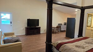 Ein Schlafzimmer mit einem Himmelbett, einem Fernseher auf einem Schrank, einem Essbereich mit Tisch und Stühlen sowie einer Küchenzeile mit Kühlschrank und Mikrowelle.