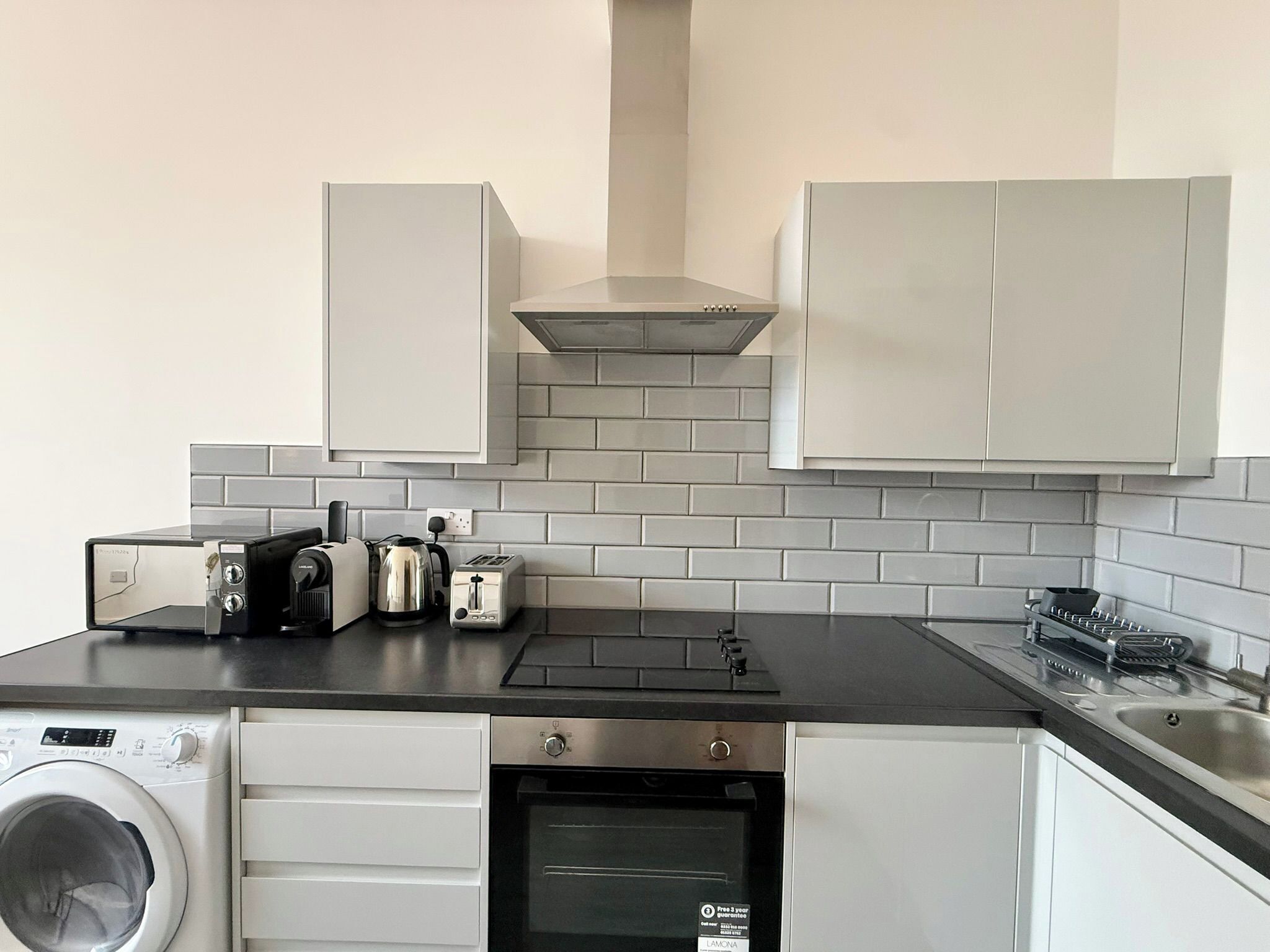 A compact kitchen with a washing machine, toaster, oven, and a stovetop.