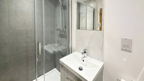 A modern bathroom with a glass-enclosed shower, a white sink, and a large mirror. - City Vibes & Comfort: 3BR Gem by Earl's Court (Greater London)