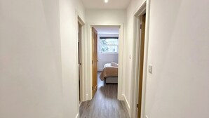 A hallway with a wooden floor, white walls, and a bed in the background. - City Vibes & Comfort: 3BR Gem by Earl's Court (Greater London)