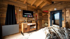 A wooden cabin interior with a television mounted on the wall, a wooden cabinet, and a large window.