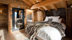 A wooden cabin bedroom with a bed, a mirror, and a stone wall.