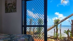 Una habitación con una cama, una puerta que da a un balcón con vistas al mar y palmeras.