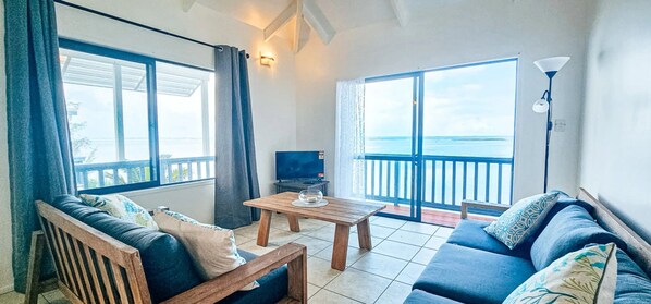 Una sala de estar con un sofá, una mesa de centro de madera, un televisor y un balcón con vista al mar.