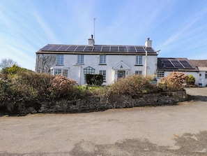 A two-story building with solar panels on the roof, a stone wall in front, and a clear sky. - Ty Crigyll (Holyhead)