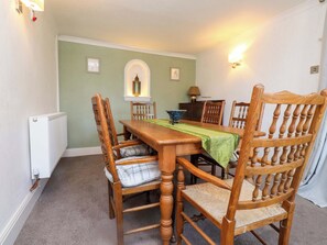 A dining room with a wooden table, chairs, a radiator, and a lamp. - Ty Crigyll (Holyhead)