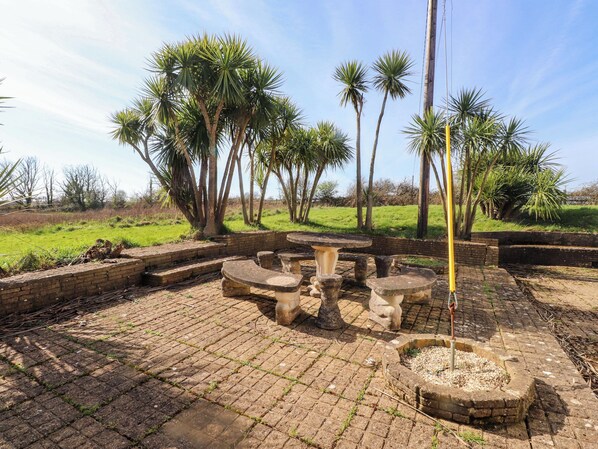 An outdoor patio area with stone tables and benches, surrounded by palm trees and a brick wall. - Ty Crigyll (Holyhead)