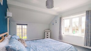 Een slaapkamer met een bed, een dressoir, een raam met gordijnen en een plafondlamp.
