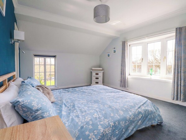A bedroom with a bed, a dresser, a window with curtains, and a ceiling light. - Ty Crigyll (Holyhead)