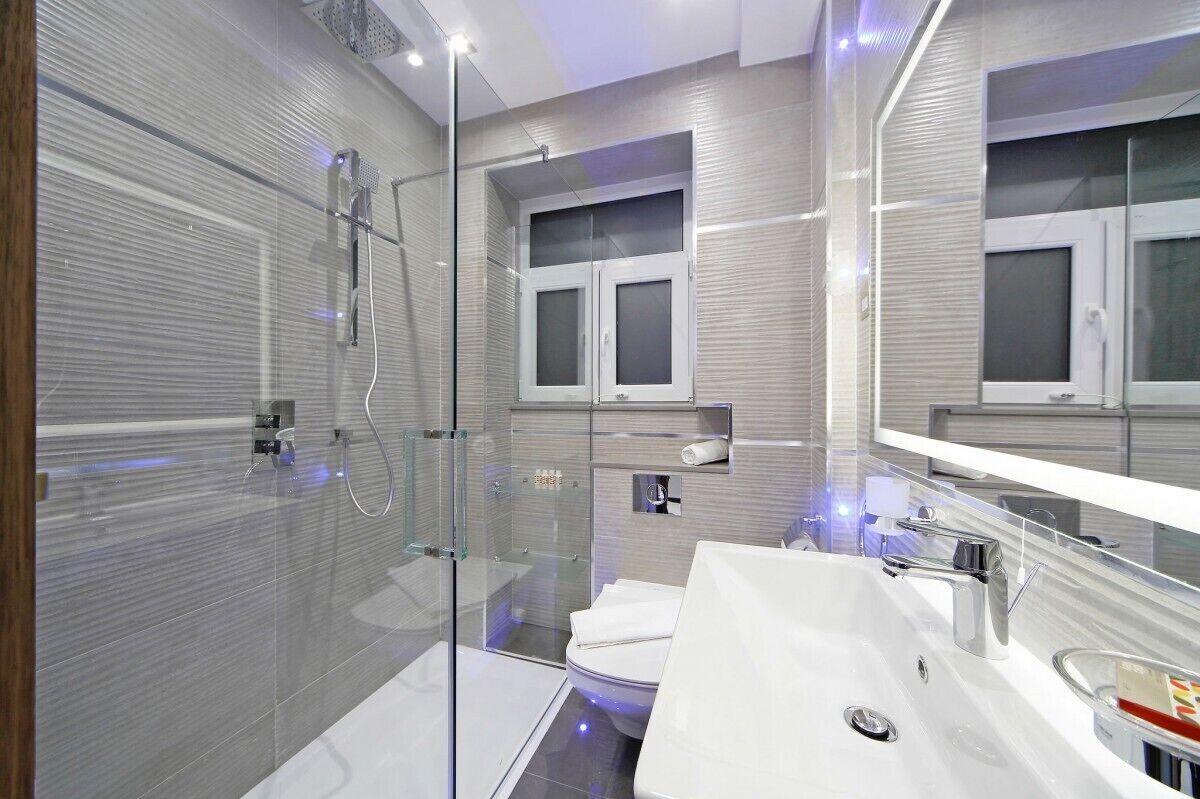 A modern bathroom with a glass shower enclosure, a white sink, and a large mirror.