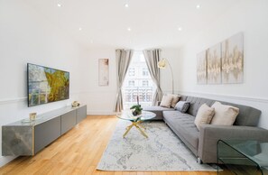 A modern living room with a grey sofa, a glass coffee table, a grey console, and a large abstract painting. - Cumberland Court (London)