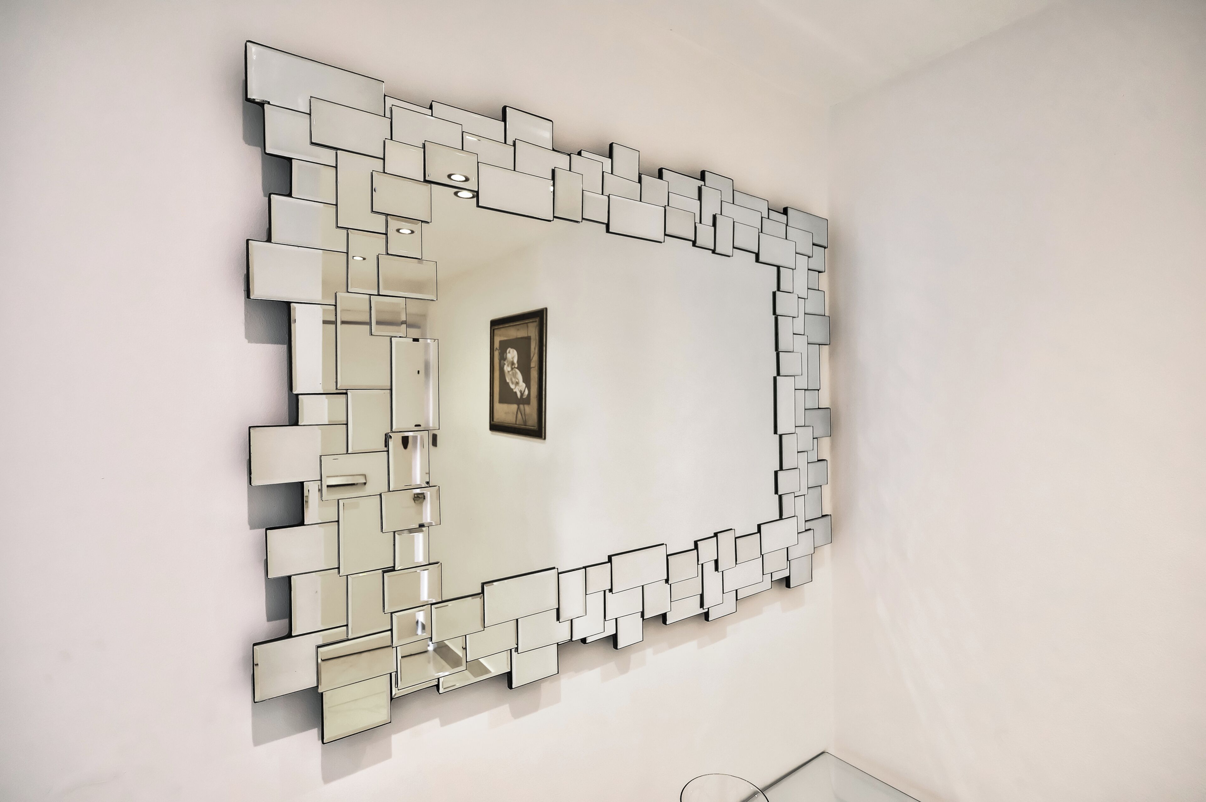 Un espejo moderno de diseño geométrico con marco blanco montado sobre una pared lisa.